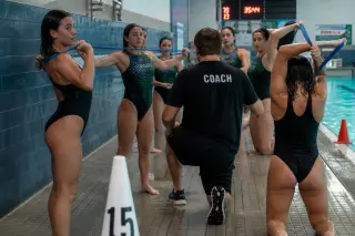 Water polo coach guiding a group of young athletes in resistance band shoulder warm-ups, poolside, with realistic, concentrated expressions and natural swimming environment.