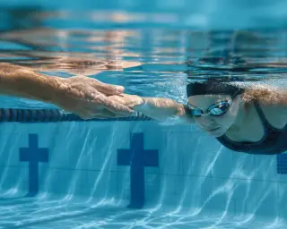 Underwater close-up of a swimmer's legs and feet gliding in breaststroke, bubbles trailing, with dappled natural light and a calm, realistic pool atmosphere.