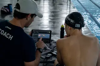 coach and swimmer reviewing swim performance data together beside a pool, with connected sports gadgets on a bench